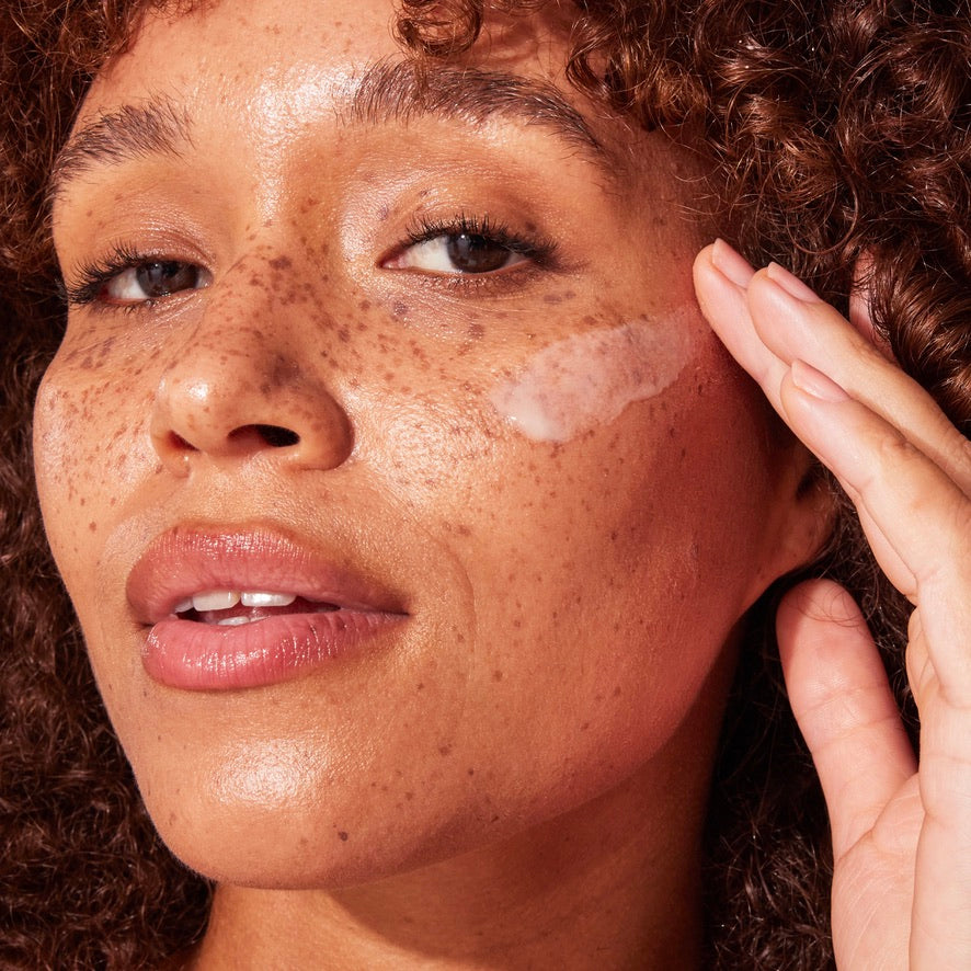 Close up of a woman applying Naked Sundays CabanaClear SPF50 Water Gel Serum to her face
