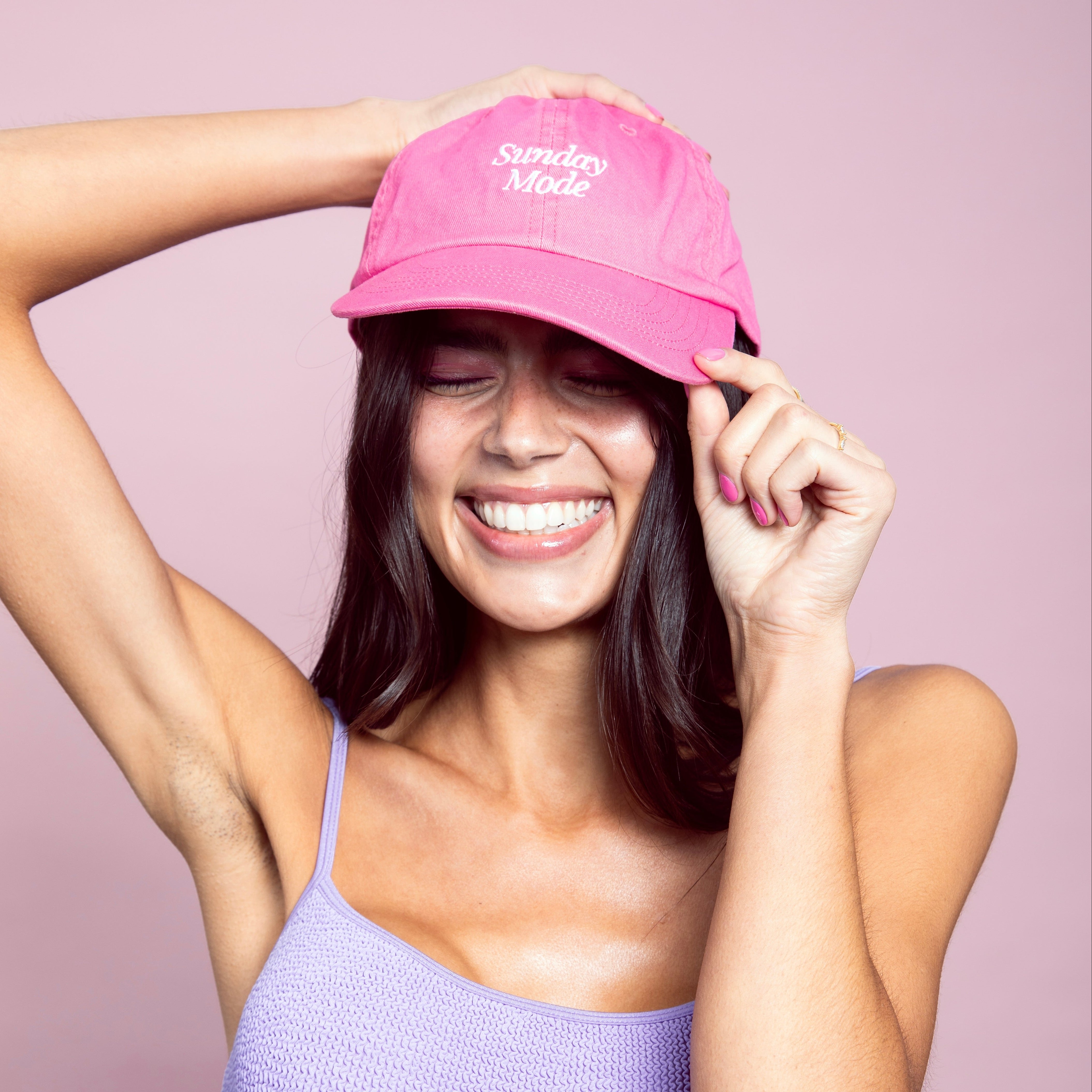 Woman wearing a pink cap with 'Sunday Mode' text on a light pink background