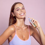 Woman applying Naked Sundays Golden Glow Shimmer Mist SPF50 to her neck with a pink background