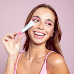 Girl holding a tube of Naked Sundays PoutScreen SPF50 Lip Treatment next to her cheek in shade Love Letter