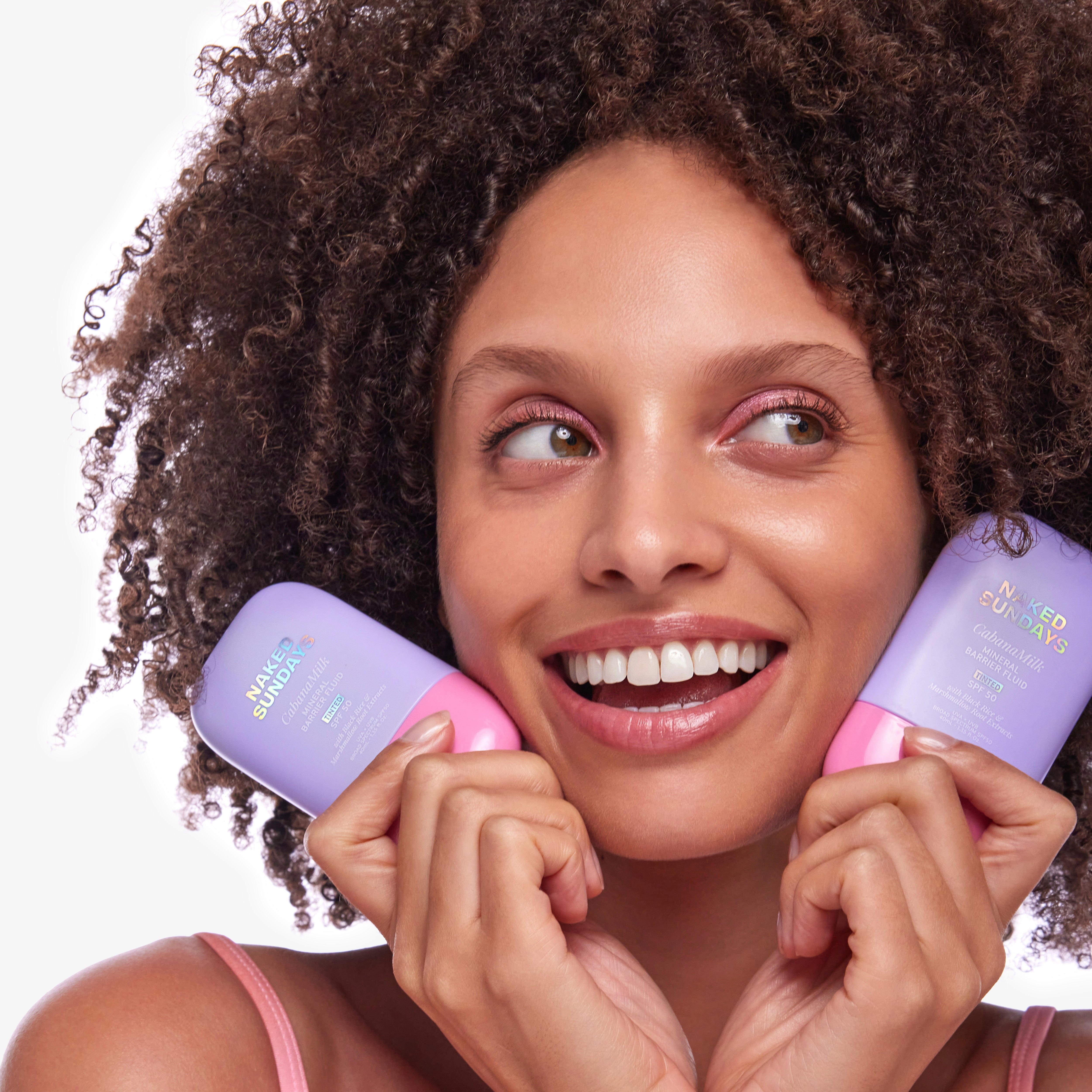 Woman holding two bottles of Naked Sundays CabanaMilk Mineral Barrier Fluid SPF50 with a white background