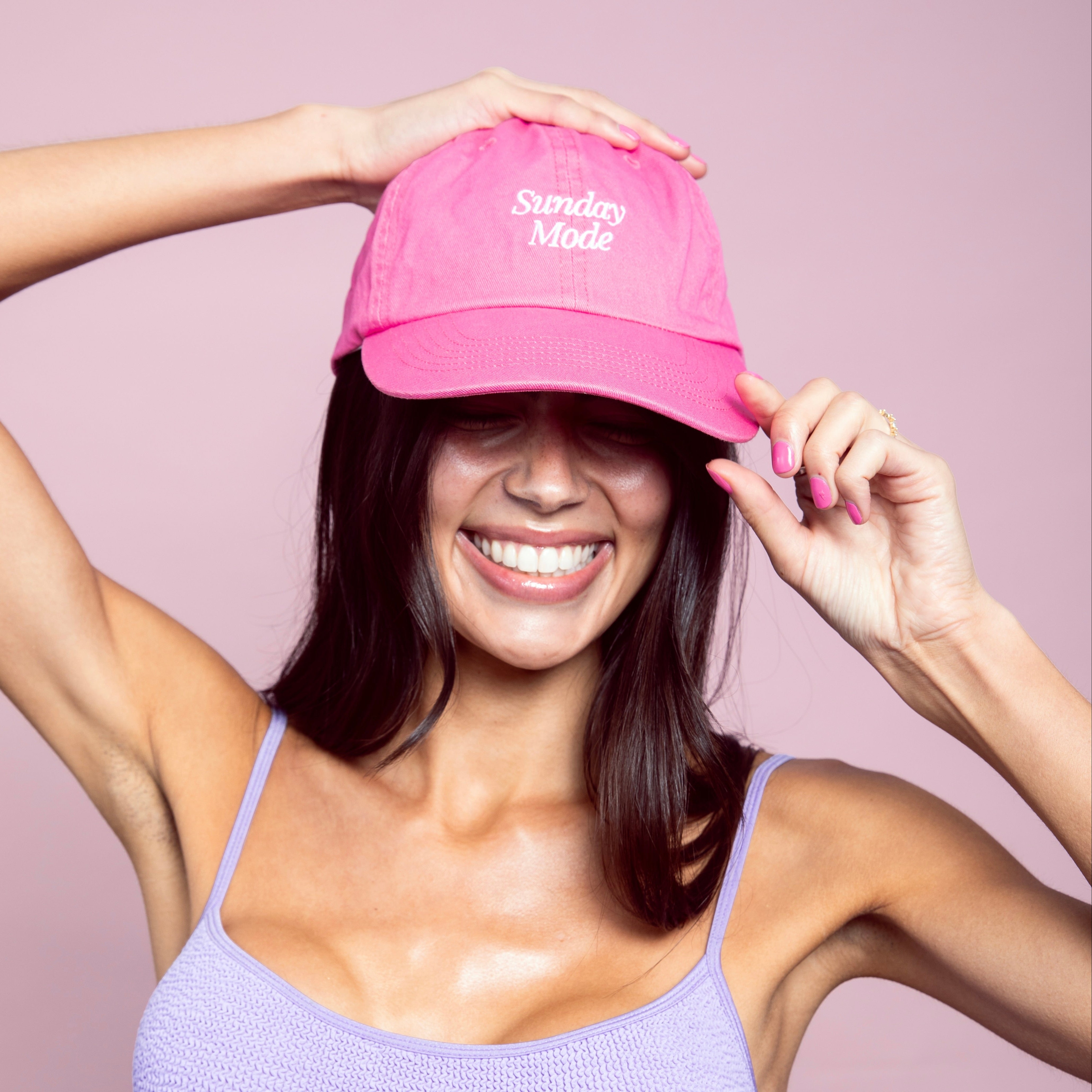 Woman wearing a pink cap with 'Sunday Mode' text on a pink background