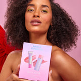 Model holding a pink Naked Sundays Rosy Glow Kit box featuring a pink SPF50 glow balm stick and lip treatment tube