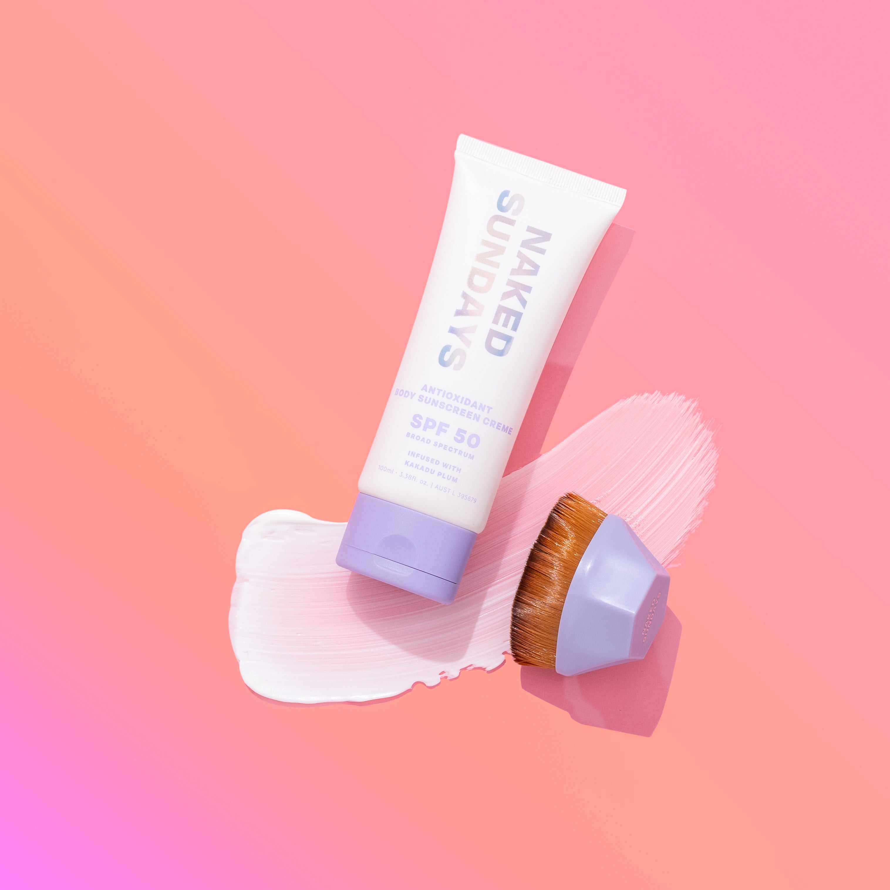 Tube of Naked Sundays Antioxidant Body Creme and an applicator brush on a pink and orange gradient background.