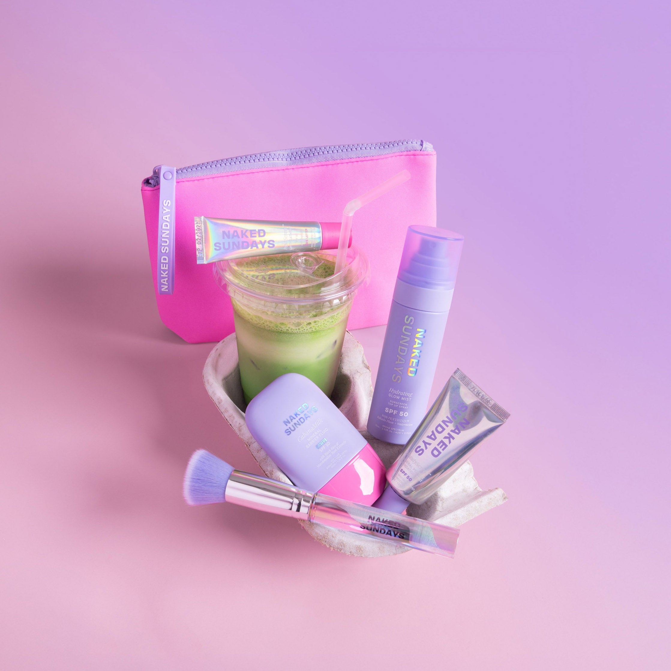Naked Sundays Bondi Sunday SPF skincare set with purple bottles, tubes, makeup brush, and pink pouch on a pink background