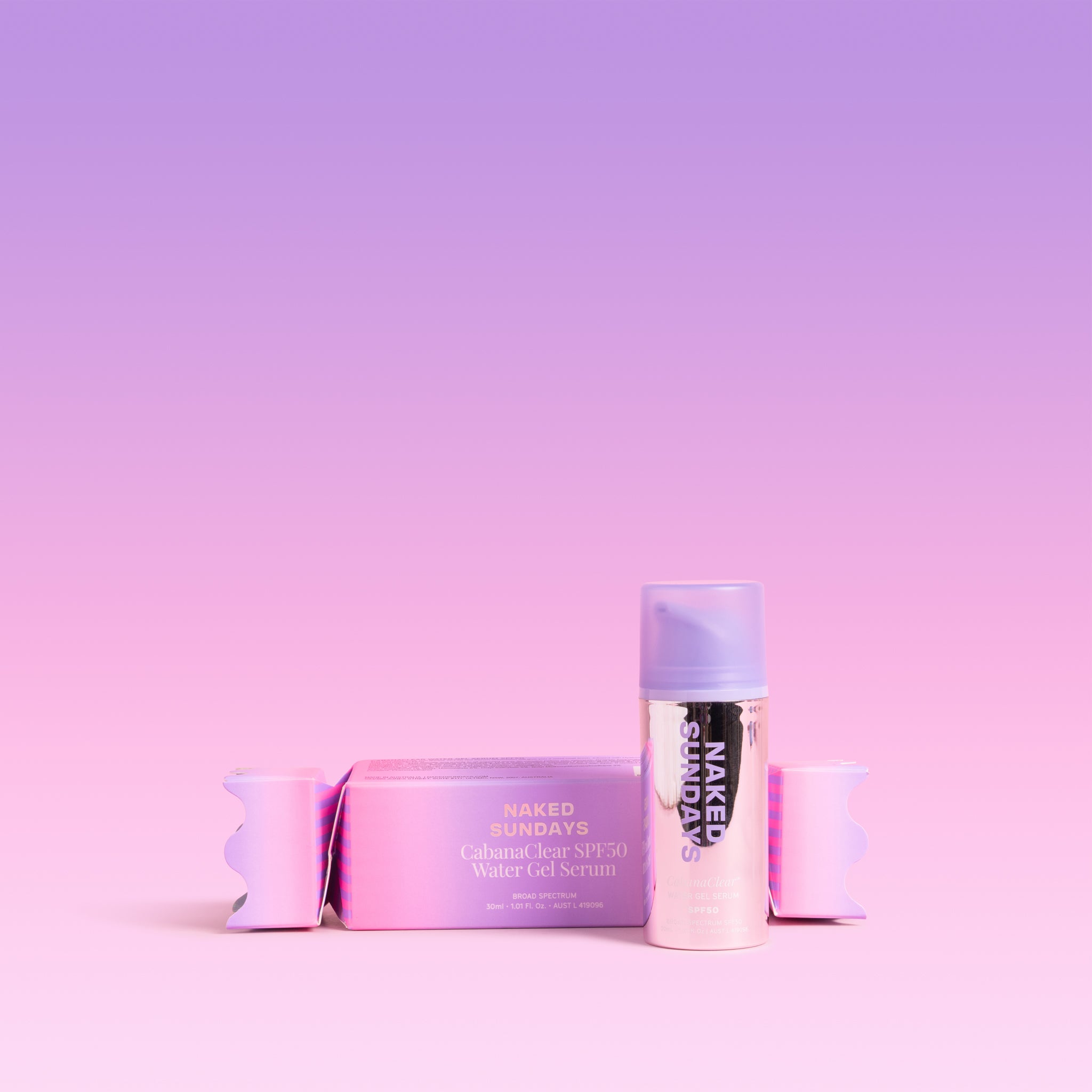 A pink and purple holiday cracker next to a bottle of Naked Sundays CabanaClear Water Gel Serum in 30mL