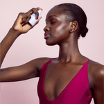 Woman applying Naked Sundays Glow Mist to her face with a pink background