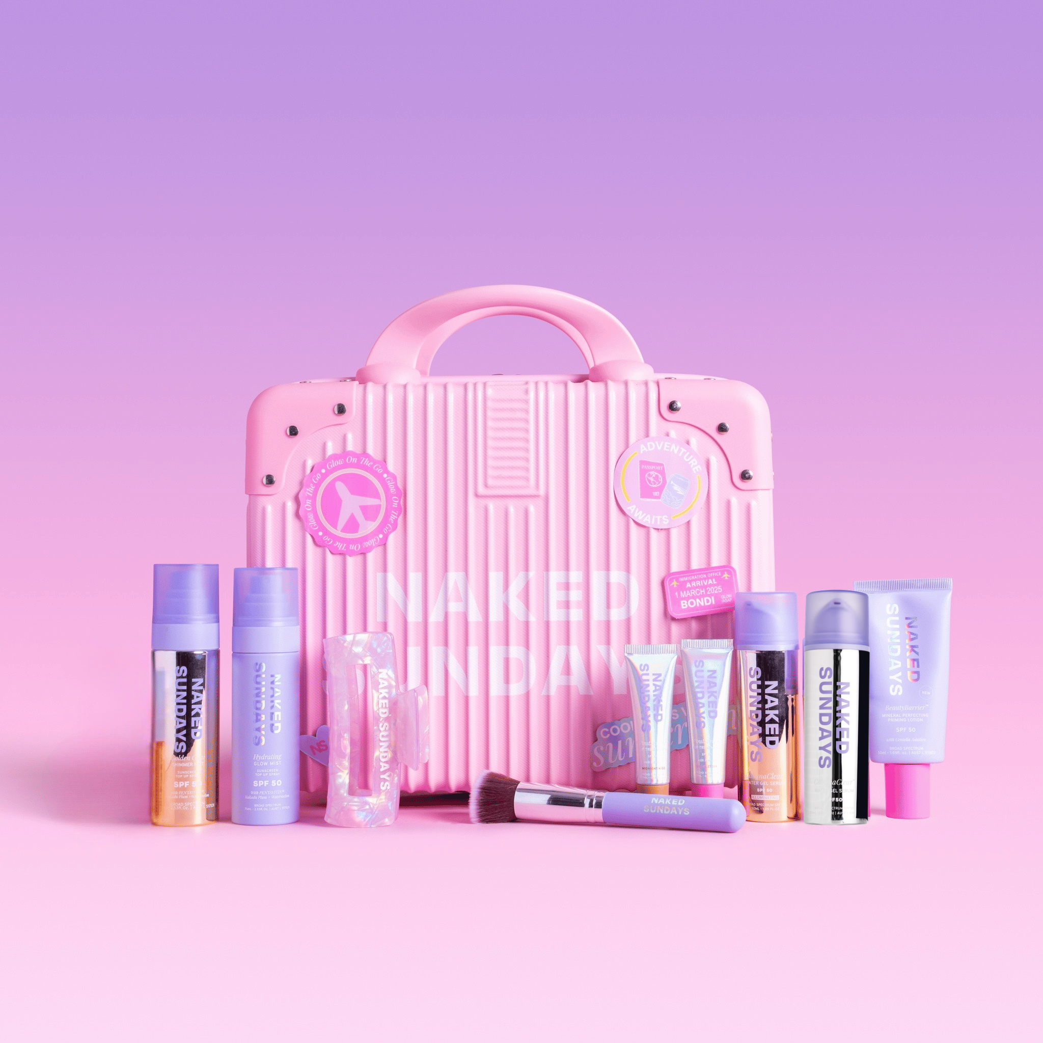A pink ribbed suitcase surrounded by multiple Naked Sundays cosmetics products and accessories on a pink and lilac gradient background