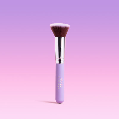 Naked Sundays SPF BFF flat-top makeup brush with a light purple handle and soft synthetic bristles against a gradient background.