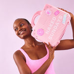 Woman in a pink swimsuit holding a pink bag with Naked Sundays branding against a light purple background