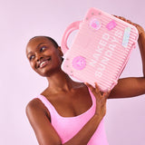 Woman in a pink swimsuit holding a pink bag with Naked Sundays branding against a light purple background