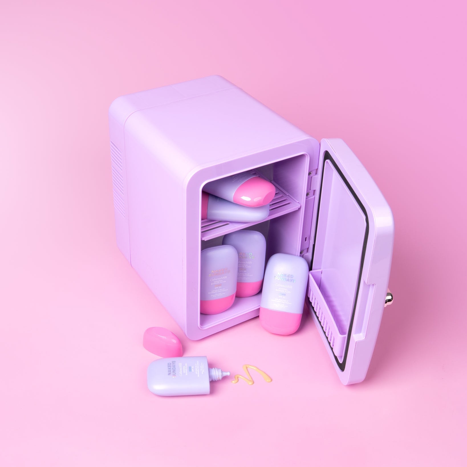 Lilac cosmetics fridge with pink and lilac Cabanamilk SPF50 bottles on a pink background