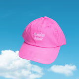 Pink cap with 'Sunday Mode' text against a blue sky with clouds