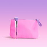A pink makeup pouch with a lavender zipper and wrist loop, shown on a soft pink to lavender gradient background