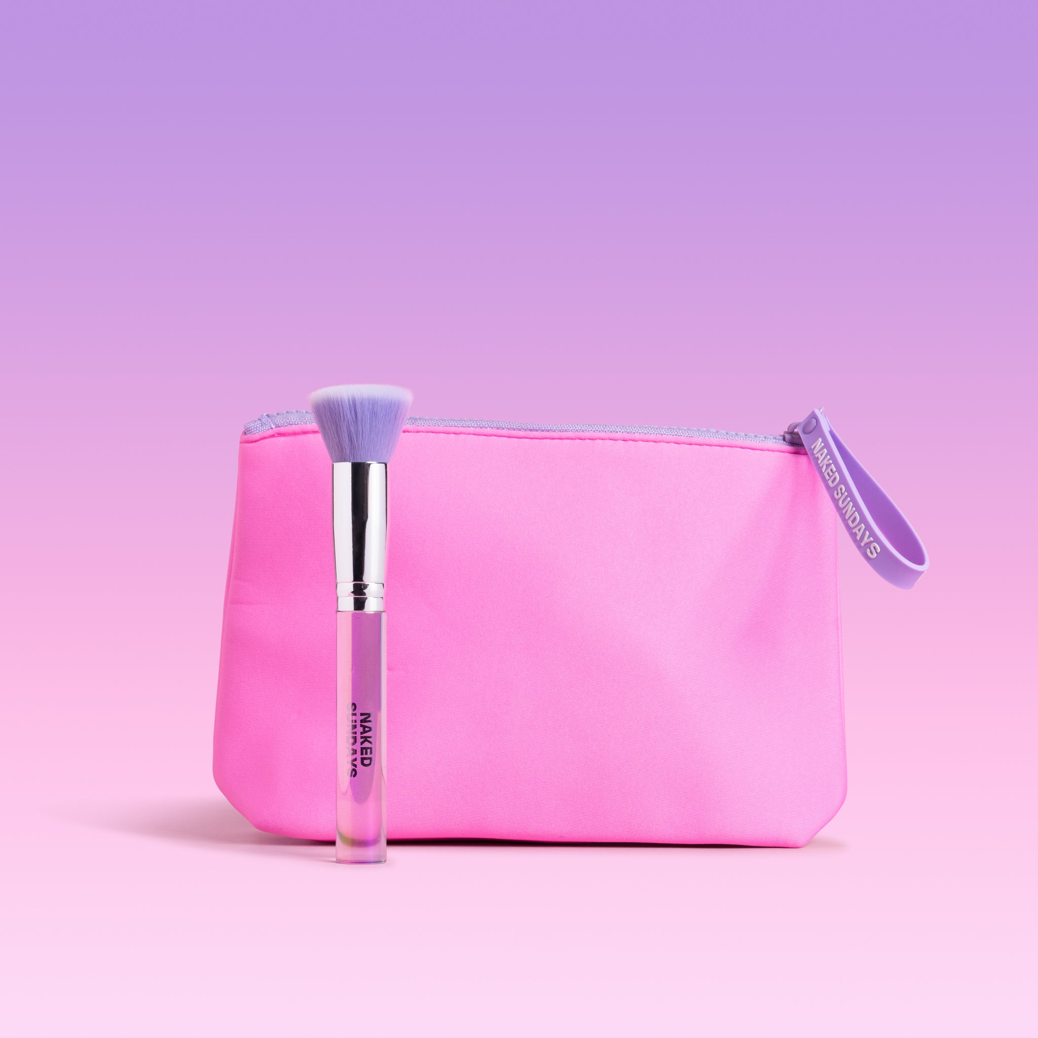 A pink makeup pouch with a lavender zipper and wrist loop, shown on a soft pink to lavender gradient background