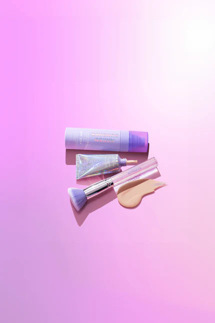 Cosmetic products including a tube, applicator, and brush on a pink gradient background