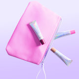 Three Naked Sundays PoutScreen lip treatments and a pink makeup bag floating on a purple background