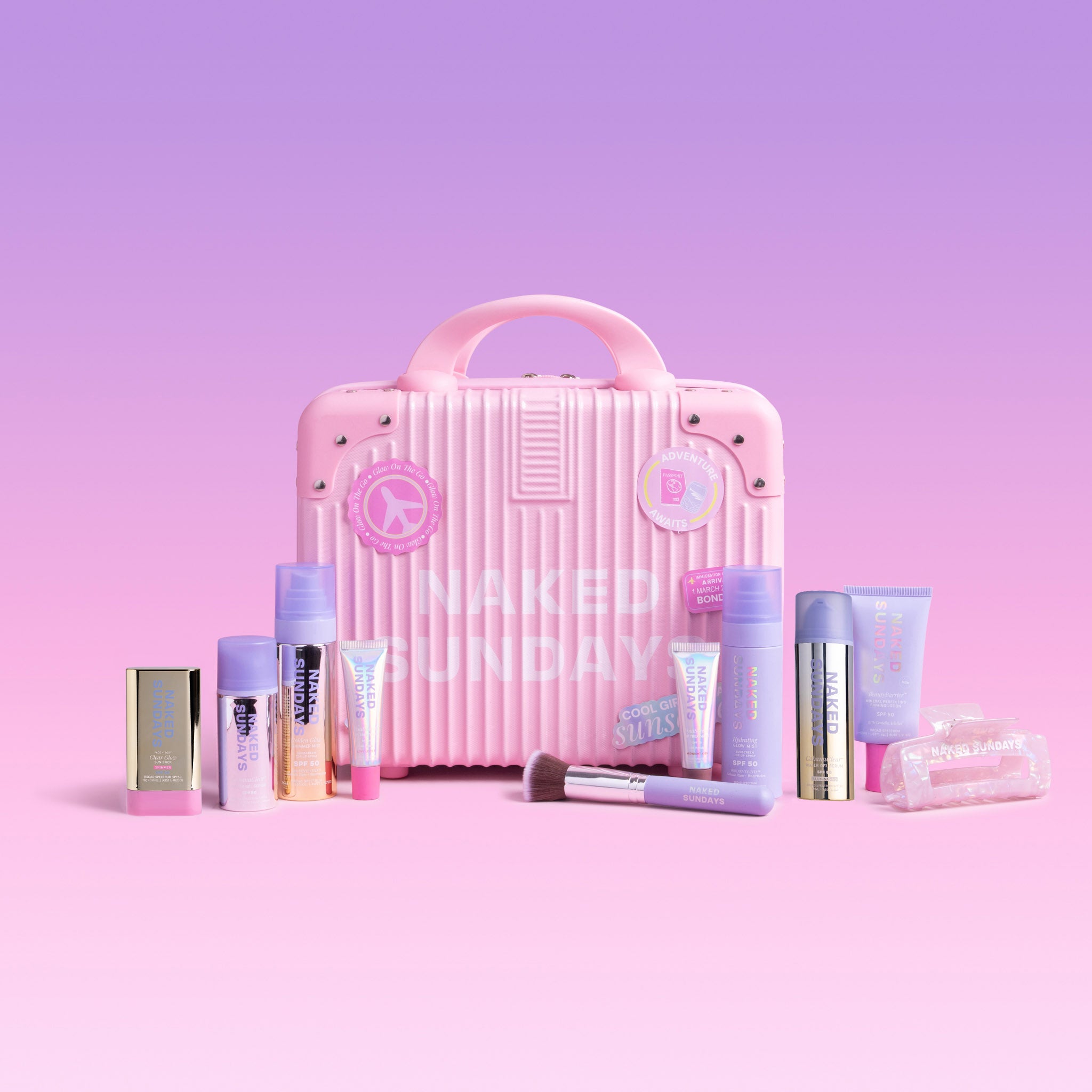 Naked Sundays First Class Jetsetter Kit featuring eight SPF skincare products and accessories in a pink carry on case