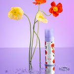 Naked Sundays x Alice & Olivia collaboration SPF50 mist with floral design next to flowers on a purple background