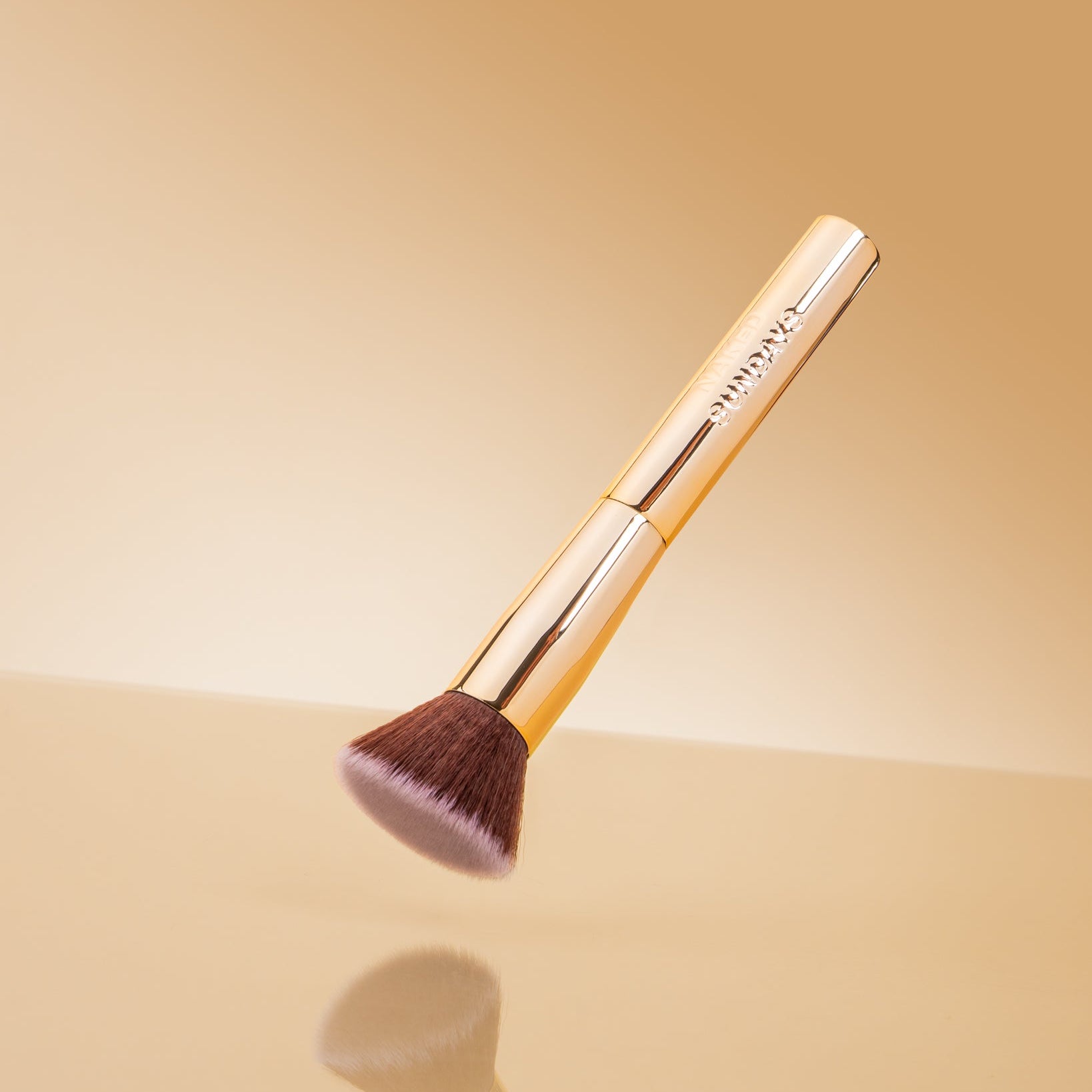 Makeup brush with gold handle and brown bristles on a beige background