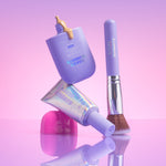 Makeup products including a bottle, brush, and tube on a reflective surface with a gradient pink to purple background