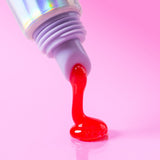 Sheer red lip treatment dripping from a holographic tube onto a vibrant pink background