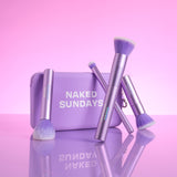 Naked Sundays makeup brushes with a purple and white box on a pink background.