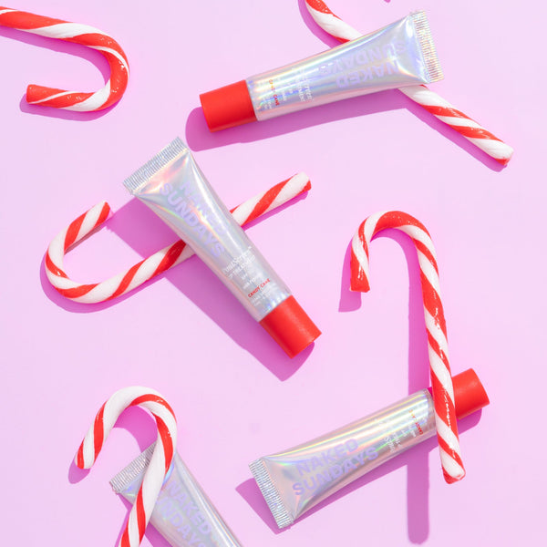  4 lip products with the label Naked Sundays Candy Cane, scattered around a pink background with candy canes.