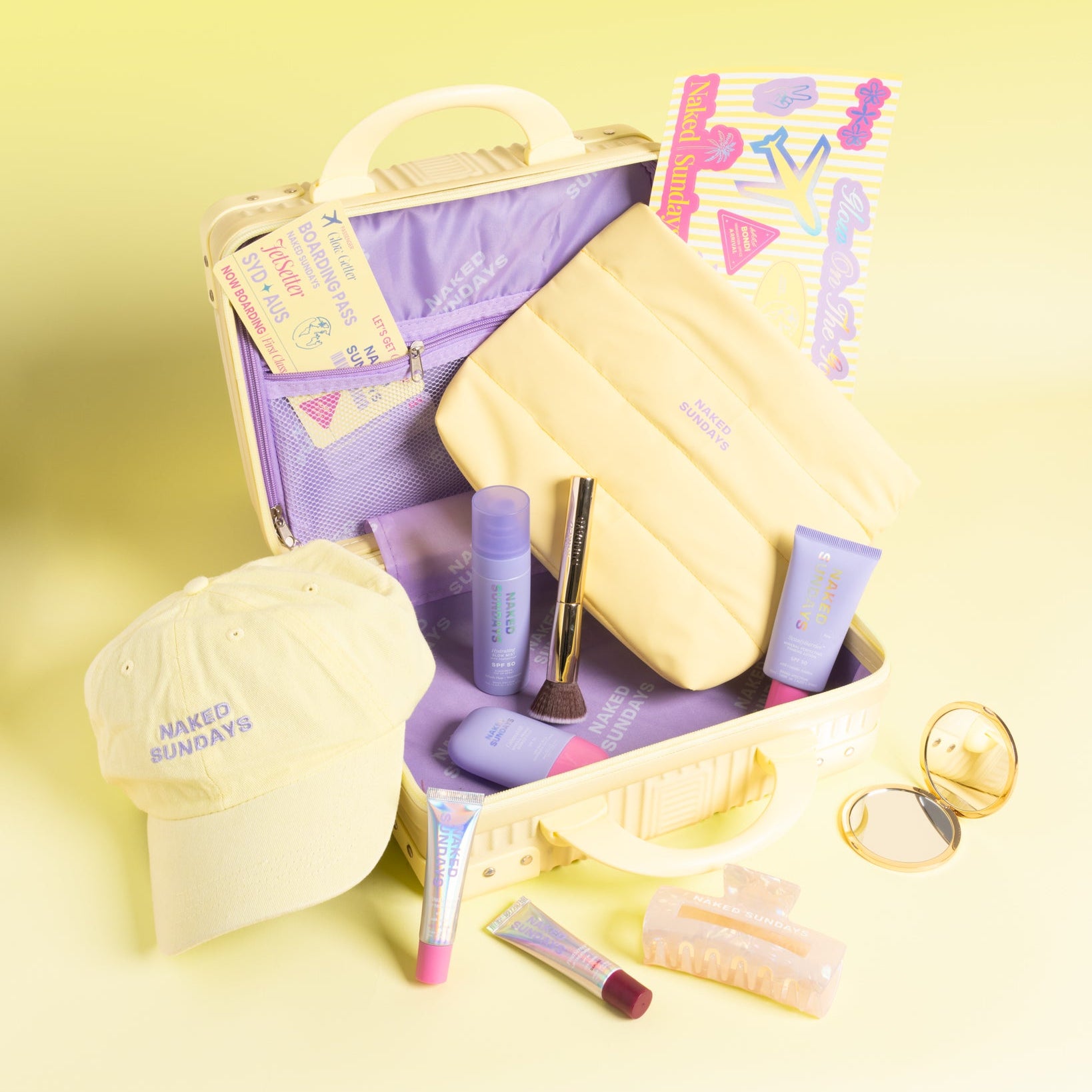 A yellow travel themed beauty gift set arranged in an open suitcase on a pale yellow background