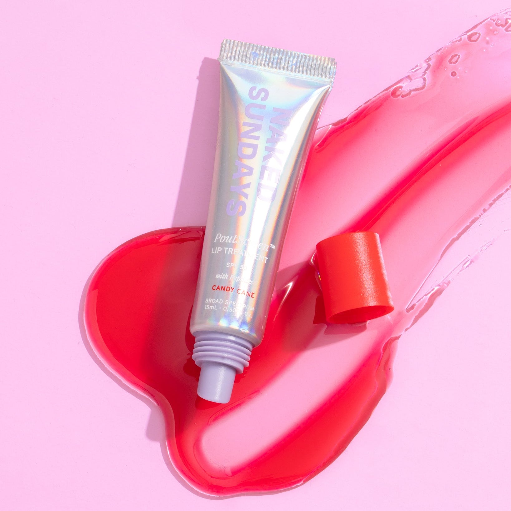 A tube of Naked Sundays Lip SPF and a red swatch of product on a pink background