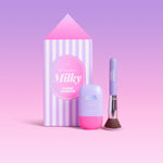 CabanaMilk SPF50 set with a striped house shaped box, mineral fluid bottle, and makeup brush in purple and pink tones