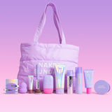 A pastel purple makeup bag with long handles sits on a pink lavender studio background, surrounded by matching cosmetic products from Naked Sundays