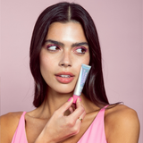 Woman holding a Naked Sundays PoutScreen Lip Treatment against a pink background